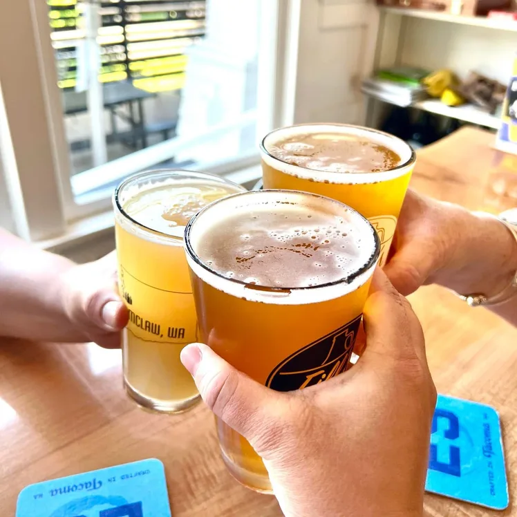 Three people touching Fill's pint glasses together in a toast at a sunlit table.