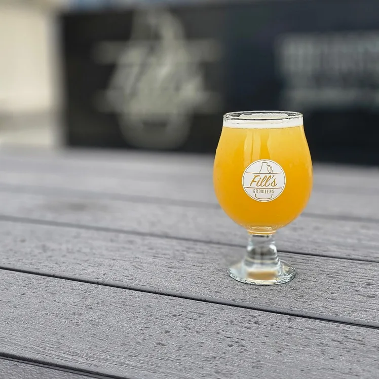 A Fill's tulip glass of hazy golden beer on a weathered grey patio table.